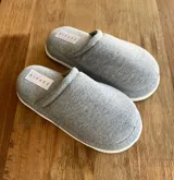 Pantuflas de dama cerradas, color gris, con plataforma blanca y etiqueta con logo en el empeine.