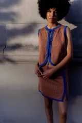 Chaleco tejido calado color camel con bordes y detalles en lurex azul brillante. Es sin mangas y tiene un escote redondo con cierre de lazos frontales.