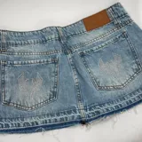 Minifalda de denim de tiro medio, color celeste con lavado ácido. Cuenta con bolsillos traseros con apliques de strass en forma de rayo, trabillas para cinturón y ruedo desmechado.
