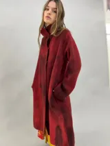 Tapado de lana merino afieltrada con diseño artesanal teñido en tonos violeta y fucsia. Presenta cuello elevado, cierre frontal con broches ocultos, bolsillos laterales y un corte ligeramente más largo en la parte trasera.