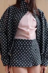 Chaqueta abullonada negra con lunares blancos, cuello subido, manga larga con puños y pliegues. Cuenta con bolsillos delanteros, bajo ajustable con cordones y cierre frontal con cremallera.