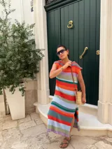 Vestido largo de tejido de punto, con rayas horizontales en tonos tierra, azul y blanco. Presenta cuello redondo, mangas cortas caídas y aberturas laterales en el ruedo.