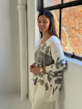 Sweater de punto con cuello en V y mangas largas, de diseño holgado. Presenta un estampado abstracto en tonos verdes con detalles metalizados en color dorado sobre una base de color crema.