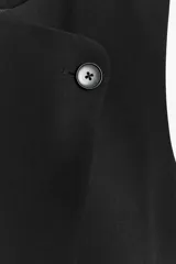 Chaleco negro de cuello redondo y sin mangas, con cierre frontal cruzado con un botón y bajo asimétrico.