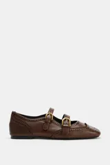 Zapato plano tipo bailarina de piel en color marrón, con detalles de perforaciones estilo brogue, doble tira delantera con hebillas metálicas doradas y puntera cuadrada.
