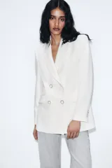 Blazer blanco de manga larga con cuello solapa y hombreras. Diseño cruzado con cierre frontal de cuatro botones y bolsillos delanteros con solapa.