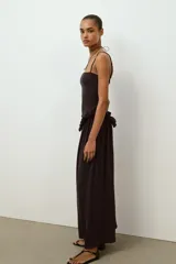 Vestido largo de color negro con escote recto y tirantes finos ajustables. Presenta un diseño con detalle de volante tipo peplum en la cintura y falda con caída fluida.