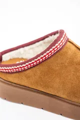Zueco de gamuza color camel con interior forrado en piel sintética. Presenta una guarda bordada decorativa en el borde superior y una suela de plataforma de goma color marrón.