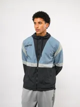 Campera de nylon Umbro con capucha, cierre frontal y diseño de bloques de color en gris, blanco y azul. Puños y dobladillo elásticos.