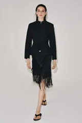 Falda corta de tiro medio, color negro, con diseño cruzado estilo pareo ajustable con lazada lateral. Cuenta con bordados tonales de motivos florales y bajo acabado con flecos largos.
