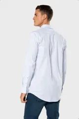Camisa Oxford lisa de color celeste, con cuello abotonado, manga larga, cierre frontal de botones y un bolsillo aplicado en el pecho con detalle bordado.