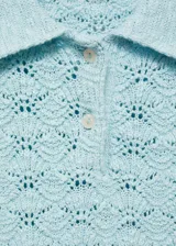 Jersey de punto crochet color turquesa, con cuello polo y cierre frontal de botones. Presenta mangas cortas y un diseño recto.