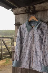 Campera de lona estampada con diseño de caballos y flores, con cuello de pana en color gris azulado y cierre frontal metálico. El interior está forrado en tela de viyela a cuadros.