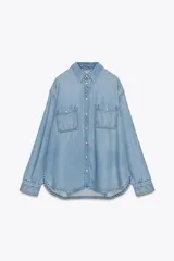 Camisa de denim de corte oversize con cuello solapa, manga larga con puños, cierre frontal con botones a presión y bolsillos de plastrón en el delantero.