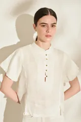 Blusa color manteca de lino, con cuello mao, mangas cortas abullonadas y cierre frontal parcial con botones dorados.