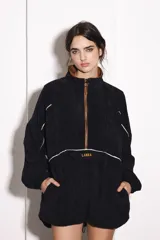 Buzo negro de pana con cuello alto y cierre marrón. Tiene bolsillo delantero con cierre, puños ajustados y ruedo regulable.