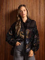 Camisa de manga larga con diseño de terciopelo estampado con motivos florales y paisley, combinada con paneles de tela transparente en la parte superior. Presenta cuello clásico, cierre frontal con botones y mangas abullonadas.