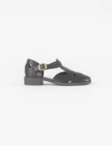 Mocasín tipo sandalia de cuero vegano color negro, con diseño calado en la parte frontal, cierre con hebilla lateral y taco bajo cuadrado.