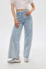 Pantalón jean de tiro alto y corte ancho, color celeste, con delicados bordados de flores blancas en la parte inferior de las piernas.