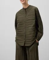 Camisa plisada color verde militar, de cuello redondo y manga larga. Tiene cierre con botones, bolsillo plastrón en el pecho y bajo redondeado.