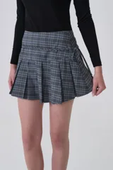 Falda corta plisada de poliéster con estampado tartán en tonos grises, azules y beige. Presenta un detalle de lazo o fajín anudado en la cintura.