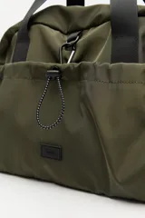 Bolso de nylon en color verde militar, con diseño deportivo, asas de mano resistentes, cierre superior y bolsillos laterales con frunce ajustable mediante cordón elástico.