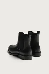 Bota estilo Chelsea de color negro, con parte superior lisa, paneles elásticos laterales y tirador trasero. Cuenta con horma redonda y suela con ligero tacón.