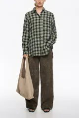 Camisa de corte recto y largo medio, confeccionada en tejido de algodón con textura. Presenta un diseño de cuadros en tonos rojo, negro y azul, cuello camisero, cierre frontal con botones, manga larga con puños abotonados y bolsillo de plastrón en el pecho.