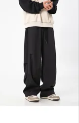 Pantalón cargo negro de corte ancho y holgado, con cintura elástica y cordón ajustable. Presenta detalles de corte o solapa en la parte trasera de las pantorrillas.