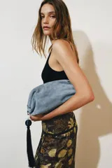 Bolso de mano tipo pouch de ante color celeste, con cierre imantado, bolsillo interior con cremallera y detalle colgante de borla con piedra.