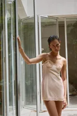 Vestido mini beige con aros de escote redondo y tirantes finos. Detalle de tejido combinado y costuras marcadas, con aplicación de encaje a tono y cierre en espalda con lazada.