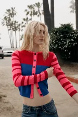 Chaqueta de punto con cuello redondo y manga larga. Presenta un diseño color block con el pecho en rojo, la parte inferior en azul y mangas a rayas horizontales en rosa y rojo. Cierre frontal con botones.