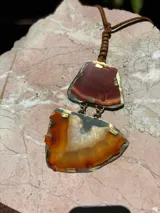 Collar con tiento de cuero marrón trenzado y dos dijes colgantes de piedras de ágata en tonos rojizos y anaranjados, engarzadas en metal dorado.