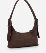Cartera tipo shoulder bag de tamaño pequeño, confeccionada en material sintético con acabado tipo gamuza y textura crocco. Presenta una correa de hombro fija con hebillas metálicas decorativas en los laterales y cierre superior por cremallera.