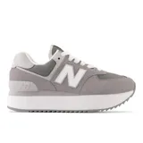 Championes urbanos New Balance modelo 574, color gris con detalles en blanco, confeccionados en gamuza y malla, con logo "N" característico en los laterales y entresuela alta de goma blanca.