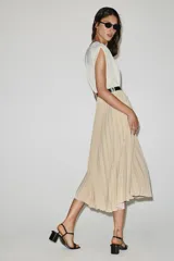 Vestido midi bicolor con parte superior blanca de escote en V cruzado con ribete negro y falda plisada en color tostado. Cuenta con mangas sisa, cintura elástica y un cinturón negro tipo reptil con hebilla ovalada.