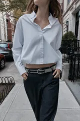 Camisa de popelín color blanco, con cuello solapa, manga larga y bajo abullonado con elástico interior. Cierre frontal con botones.