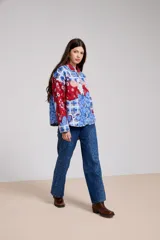 Campera de estilo camisa con diseño capitoneado y estampado patchwork que combina motivos florales, paisley y cuadros en tonos rojos y azules. Presenta cuello camisero, cierre frontal con botones y bolsillos delanteros.