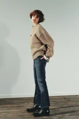 Jeans de tiro alto color marrón oscuro con acabado lavado, corte recto/flare y bajo cropped sin costuras. Presenta cinco bolsillos y cierre frontal con cremallera y botón metálico.