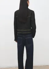 Chaqueta corta confeccionada en tejido texturizado con mezcla de algodón, poliéster y lana. Presenta cuello solapa, mangas largas, bolsillos frontales con solapa y cierre mediante botones metálicos dorados. Los bordes cuentan con detalles de flecos deshilachados.