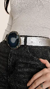 Cinturón de cuero metalizado plateado con una gran hebilla circular de piedra ágata natural en tonos azules y blancos con detalles metálicos dorados.