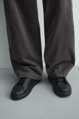 Zapatilla negra de cordones, con parte superior lisa y cordonera oculta. Posee suela con volumen a tono.