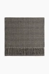 Bufanda de tejido grueso con patrón Príncipe de Gales en tonos beige y negro. Presenta flecos en los bordes cortos.