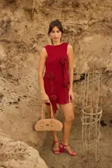 Vestido corto de tejido de punto con lúrex, sin mangas y cuello a la base. Presenta apliques decorativos en forma de flores en el frente y un pequeño tajo en el ruedo.