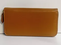 Billetera rectangular de cuero color tostado, con cierre perimetral y tirador de cuero. Interior forrado en tela roja con múltiples compartimentos para tarjetas, documentos, billetes y bolsillo con cierre para monedas.