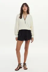Sweater de tejido de punto color blanco marfil, con calce relajado, mangas largas levemente abullonadas, escote en V con botones y detalles de ribetes en color negro.