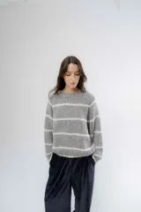 Buzo de tejido de punto grueso en color gris con rayas horizontales en color crema, de corte holgado, cuello redondo y mangas largas.