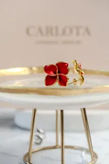 Aros con diseño de flor abierta de cuatro pétalos en color rojo con bordes dorados, fabricados en acero quirúrgico con baño de oro.