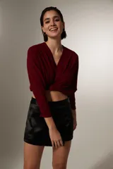 Blusa cropped de color negro, con cuello en V, mangas largas con puños ajustados y detalle de frunces en el frente.