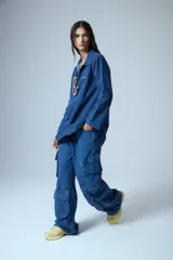 Pantalón tipo cargo de jean azul con corte oversize y tiro medio. Presenta múltiples bolsillos laterales y delanteros con solapa, confeccionado en algodón.